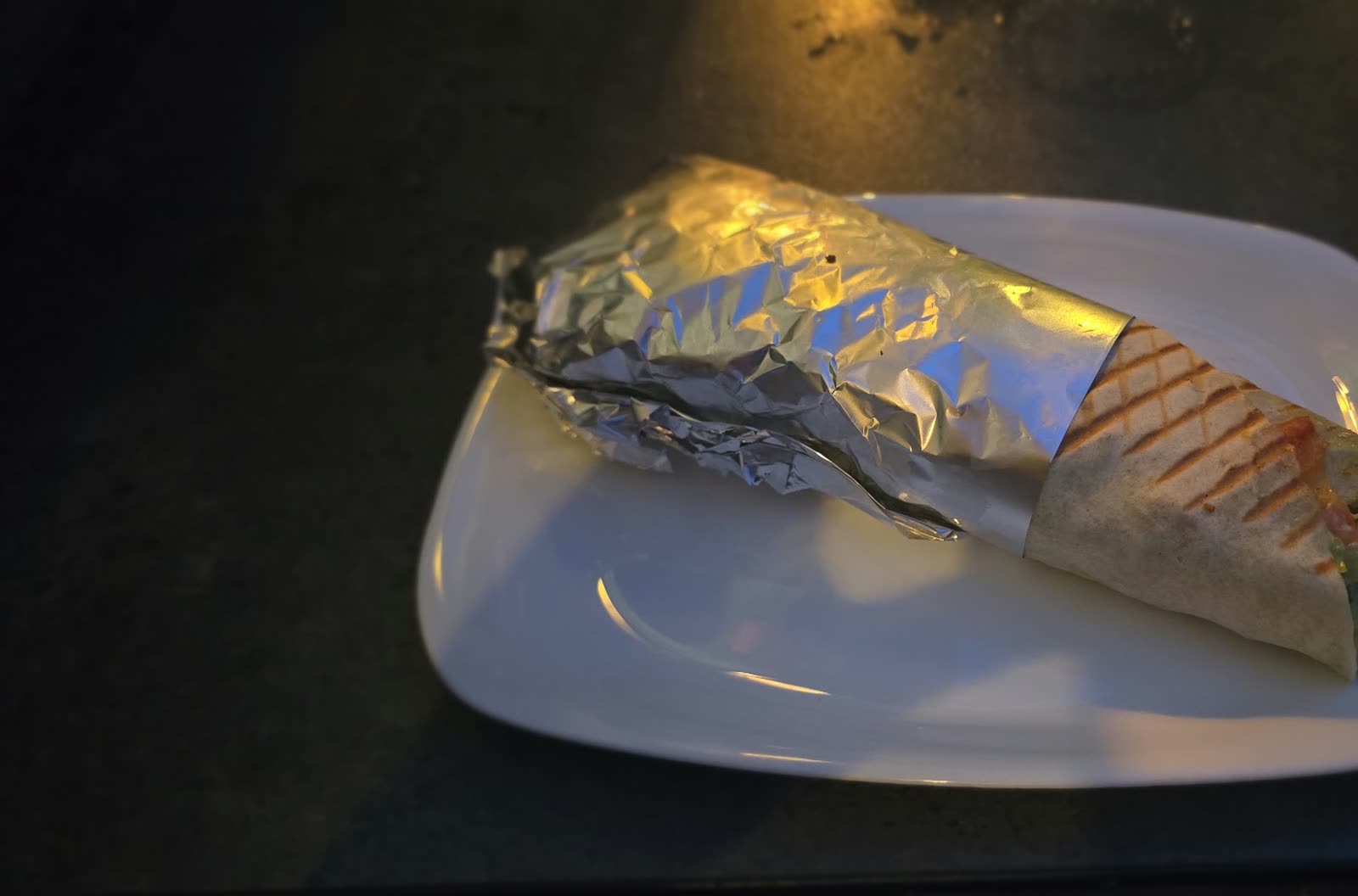 Een d&uuml;r&uuml;m van de grill op een wit bord, half in aluminiumfolie gewikkeld.