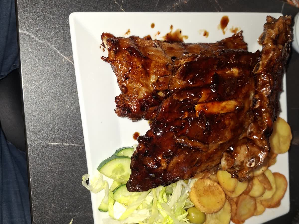 Een spareribsschotel met aardappelschijfjes en salade op een wit bord.